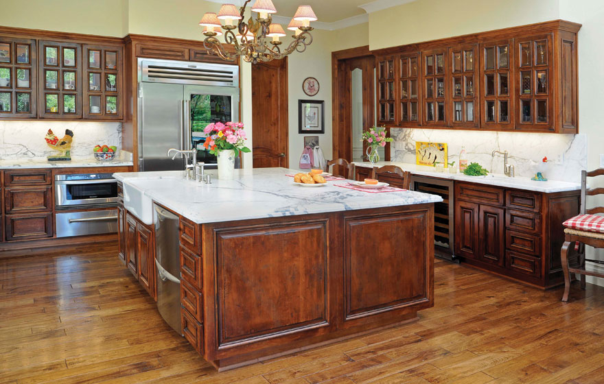 French Lite upper cabinets dazzle this kitchen where the rustic hand-distressed cabinetry contrasts the elegant marble countertops.